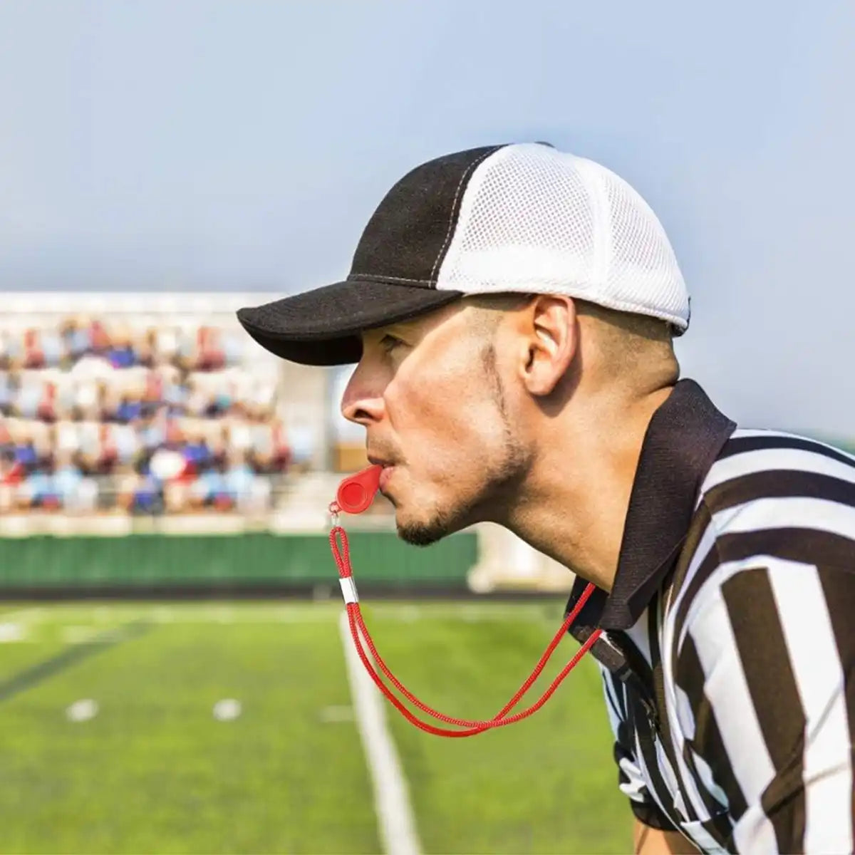 Scheidsrechter met rood noodfluitje 120dB en nylon nekkoord, gebruikt op sportveld tijdens wedstrijd