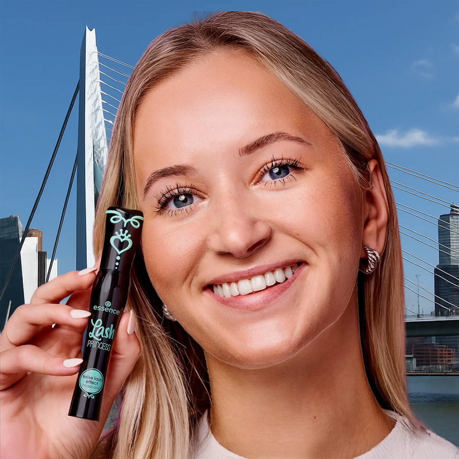 Blonde vrouw die Essence Lash Princess mascara toont met de Erasmusbrug in Rotterdam op de achtergrond